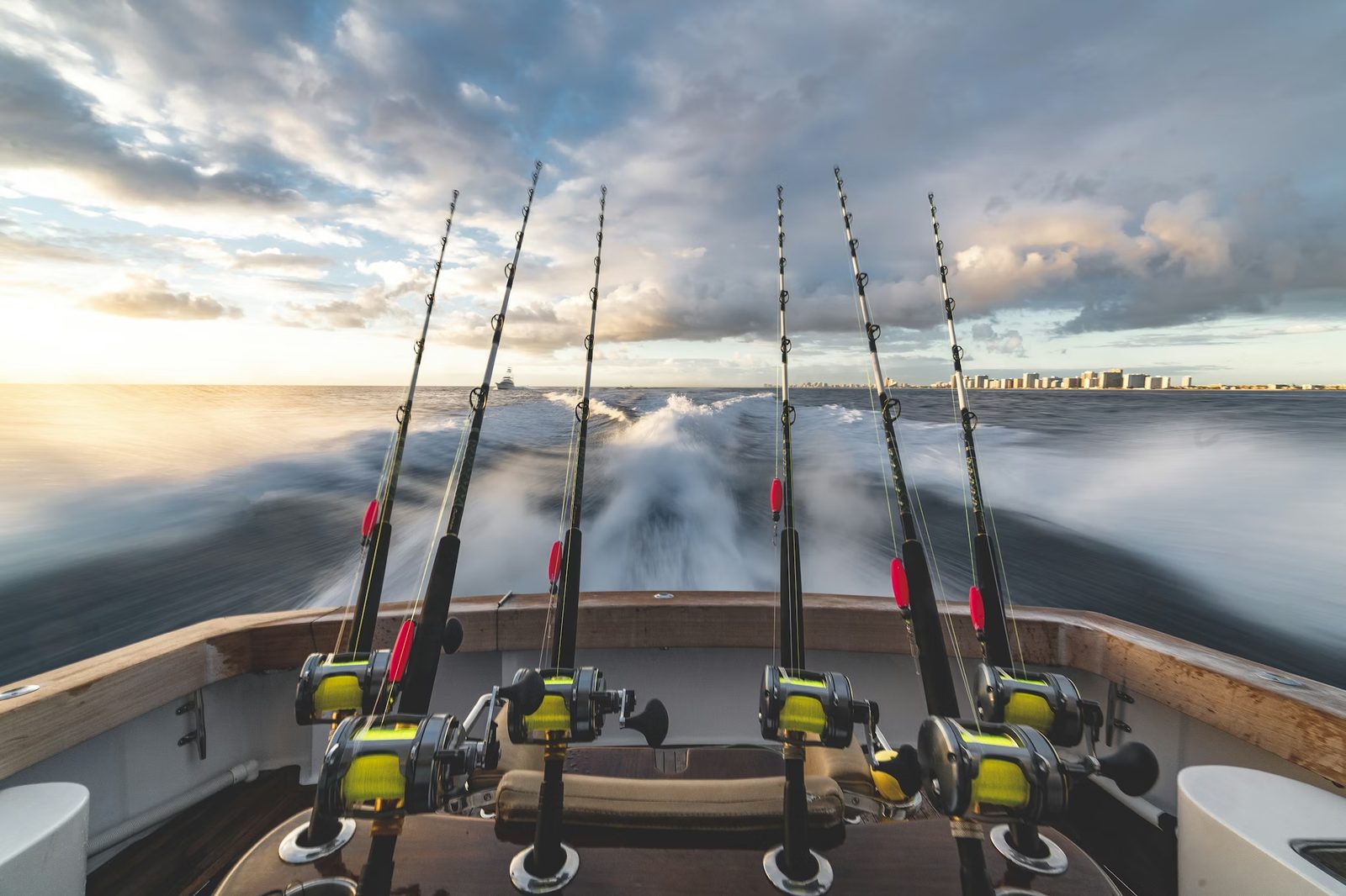 Sport fishing rods racked at the stern of a charter boat with churning wake behind